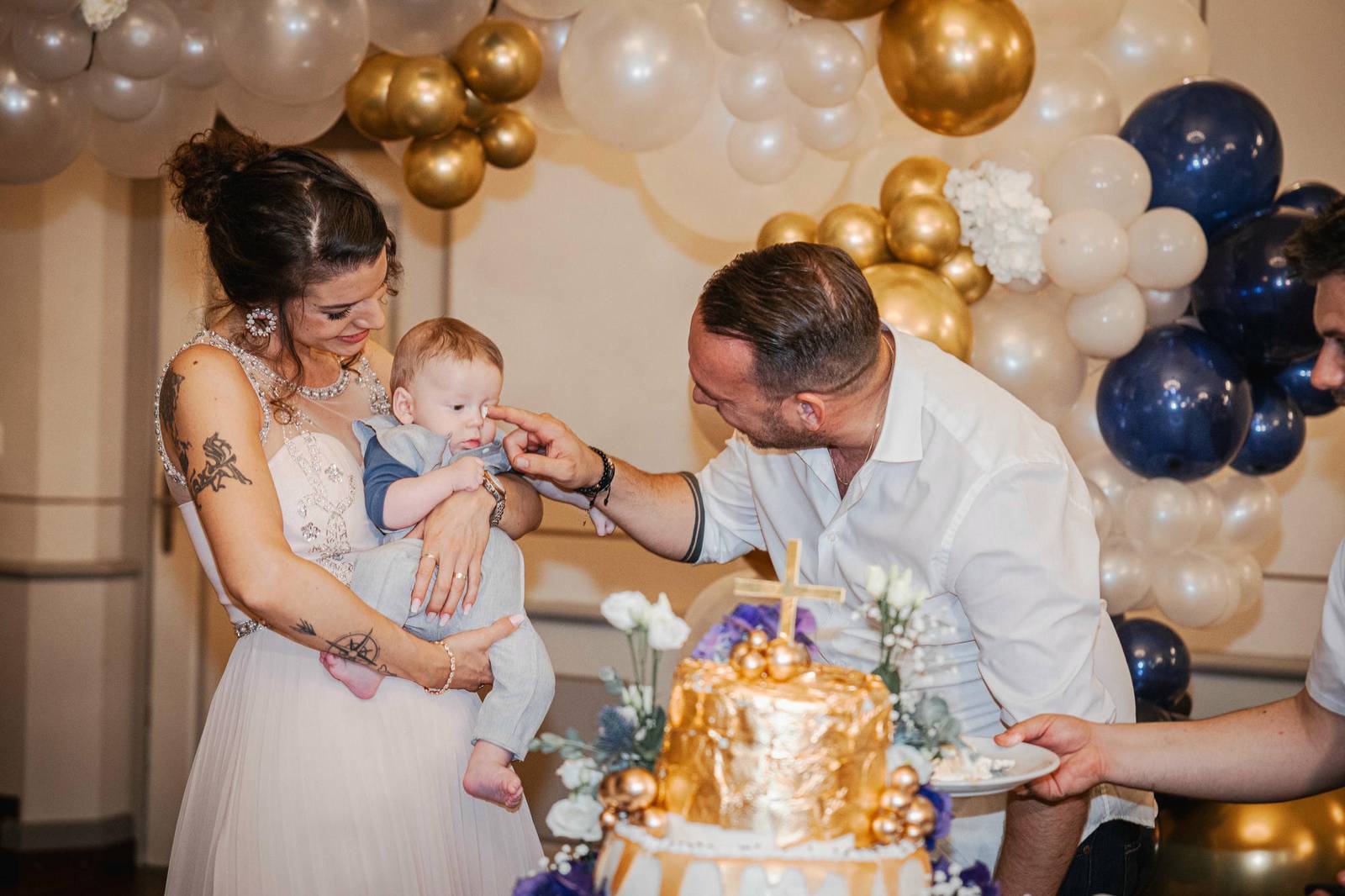 Glückliche Eltern und Baby bei einer Tauffeier, die goldene Torte im Hintergrund